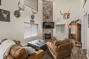 Living area featuring a stone fireplace, baseboards, a high ceiling, and wood finished floors
