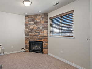 Home office featuring carpet, baseboards, a textured ceiling, visible vents, and a stone fireplace