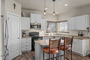 Kitchen with light countertops, a breakfast bar, appliances with stainless steel finishes, white cabinetry, and dark wood-style floors