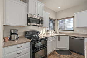 Kitchen with white cabinets, light countertops, appliances with stainless steel finishes, a sink, and dark wood-style floors