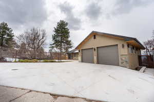 View of side of home with fence, concrete driveway, stone siding, and stucco siding