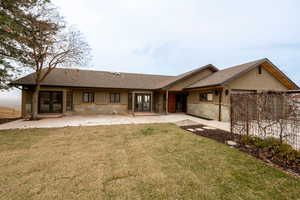 Rear view of property featuring fence, a yard, an attached garage, french doors, and stone siding