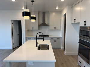 Kitchen with light countertops, stainless steel appliances, wall chimney exhaust hood, a sink, and light wood-style floors
