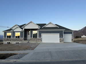 Craftsman-style home with stone siding, a garage, concrete driveway, a shingled roof, and a mountain view