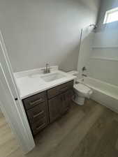 Bathroom with toilet, wood finished floors, vanity, and shower / bath combination