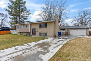 Raised ranch featuring fence, an attached garage, a chimney, concrete driveway, and a front lawn