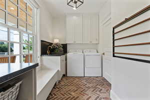 Washroom featuring a sink, cabinet space, brick floor, and washer and clothes dryer