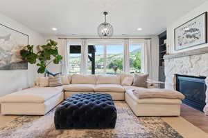 Living room with built in shelves, wood finished floors, a stone fireplace, recessed lighting, and an inviting chandelier
