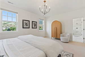 Bedroom with light colored carpet, an inviting chandelier, baseboards, ensuite bath, and visible vents