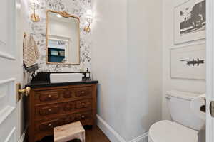 Bathroom featuring baseboards, wallpapered walls, toilet, and vanity
