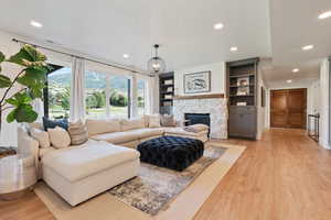 Living room with light wood finished floors, a textured ceiling, a stone fireplace, visible vents, and recessed lighting