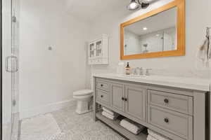 Bathroom featuring baseboards, toilet, tile patterned floors, vanity, and a stall shower