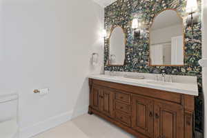 Full bath featuring toilet, a sink, baseboards, wallpapered walls, and double vanity