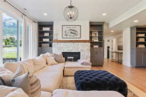 Living area featuring recessed lighting, an inviting chandelier, built in shelves, light wood finished floors, and a stone fireplace