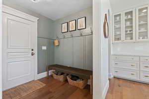 Mudroom with a textured ceiling, a decorative wall, light wood-style floors, and wainscoting