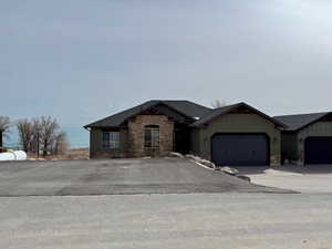 View of front of home featuring stone siding, concrette driveway, & paved parking