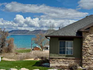 View of home's exterior featuring a water and mountain view, board and batten siding, roof with shingles, and stone siding