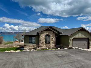 Ranch-style home with a garage, stone siding, a shingled roof, a water view, and driveway