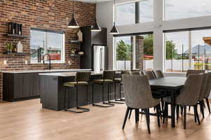 Dining area with a towering ceiling, brick wall, a healthy amount of sunlight, and light wood finished floors