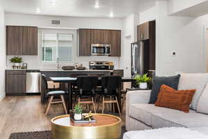 Kitchen with light wood-type flooring, a sink, modern cabinets, dark brown cabinets, and appliances with stainless steel finishes