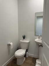 Half bath featuring baseboards, toilet, and wood finished floors
