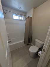 Bathroom featuring toilet, shower / tub combo with curtain, and a textured ceiling