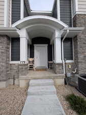 Entrance to property with stone siding, cooling unit, and covered porch