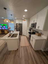 Kitchen with dark wood-type flooring, a kitchen island with sink, a sink, and appliances with stainless steel finishes