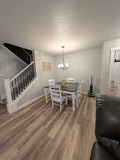 Dining space with light wood finished floors, a notable chandelier, stairs, and a textured ceiling