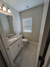Bathroom featuring toilet, vanity, wood finished floors, baseboards, and visible vents