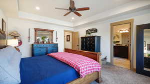 Bedroom with carpet flooring, connected bathroom, ceiling fan, recessed lighting, and a tray ceiling