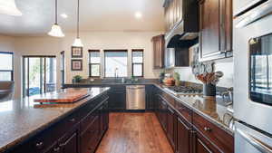Kitchen featuring dark wood finished floors, decorative light fixtures, dark stone countertops, and stainless steel appliances