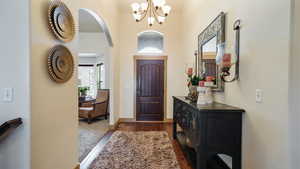 Entrance foyer with arched walkways, dark wood-style floors, baseboards, and a notable chandelier