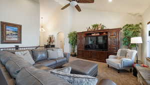 Carpeted living room featuring high vaulted ceiling, arched walkways, and ceiling fan with notable chandelier