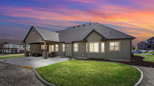 Rear view of house with stucco siding, a shingled roof, a patio, and a yard
