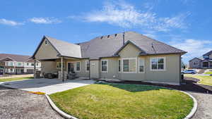 Back of house with a shingled roof, stucco siding, a yard, and a patio area