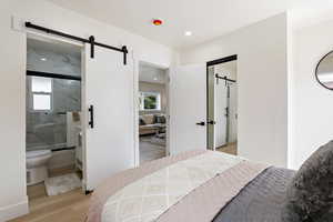 Bedroom with ensuite bath, a barn door, light wood-style flooring, and recessed lighting