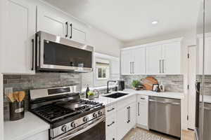 Kitchen with white cabinetry, light countertops, a sink, and appliances with stainless steel finishes