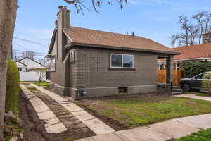 Bungalow with roof with shingles, brick siding, fence, and a chimney