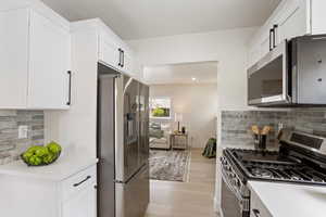 Kitchen featuring light countertops, backsplash, light wood finished floors, white cabinetry, and appliances with stainless steel finishes