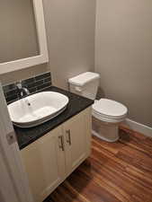 Bathroom featuring toilet, vanity, decorative backsplash, and wood finished floors