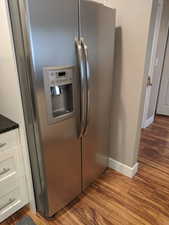 Details featuring stainless steel fridge with ice dispenser, baseboards, white cabinetry, and wood finished floors.