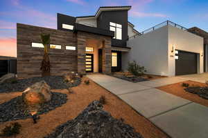 Contemporary home with a balcony, stone siding, a garage, and stucco siding
