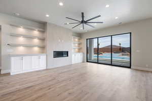 Unfurnished living room with a tile fireplace, a ceiling fan, light wood finished floors, baseboards, and visible vents