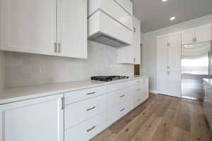 Kitchen with white cabinetry, light wood-style flooring, custom exhaust hood, and appliances with stainless steel finishes
