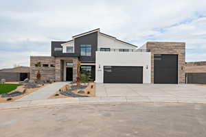 Modern home featuring stone siding, an attached garage, concrete driveway, and stucco siding