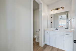 Bathroom with toilet, vanity, a ceiling fan, wood finished floors, and baseboards