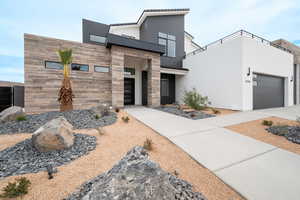 Contemporary house featuring stone siding, concrete driveway, stucco siding, an attached garage, and a balcony