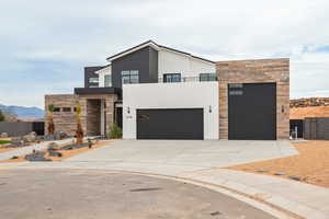 Contemporary home with stone siding, concrete driveway, stucco siding, an attached garage, and a balcony