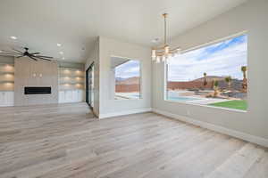 Unfurnished dining area with a tile fireplace, wood finished floors, baseboards, ceiling fan with notable chandelier, and recessed lighting